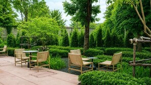 An outdoor seating area with wicker chairs and a round table, surrounded by well-maintained hedges and trees. - Go Hotel Chiang Rai (Chiang Rai)