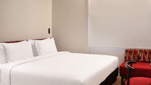 A hotel room with a bed, a chair, and a wall-mounted light fixture. - Go Hotel Chiang Rai (Chiang Rai)