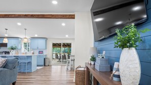 Une cuisine moderne avec des meubles bleus, un plafond en bois et un grand téléviseur.