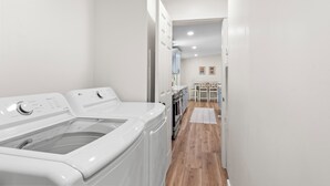 Une buanderie équipée d’un lave-linge et d’un sèche-linge à chargement frontal, un coin repas avec une table et des chaises, et une cuisine avec un four et un réfrigérateur.