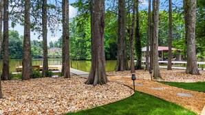 Un cadre paisible au bord d’un lac, avec une jetée en bois, entouré de grands arbres et de sentiers de gravier.