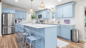 Une cuisine moderne avec des meubles de couleur bleu clair, des appareils en acier inoxydable et un îlot central doté de tabourets de bar.