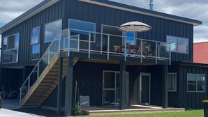 Une maison moderne à deux étages, dotée d’un balcon, de grandes fenêtres et d’un escalier menant à l’étage supérieur.