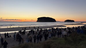 Une plage où se sont rassemblées des personnes, une grande formation rocheuse à l’horizon et un ciel dégagé.
