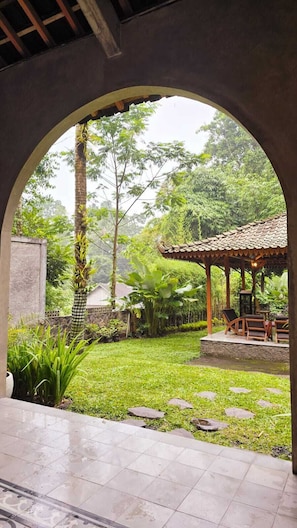 A covered outdoor area with a stone bench, a pergola, and a view of a lush garden. - nDalem Riyartan Villa Kaliurang (Sleman)