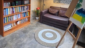 Una habitación con una estantería, un sofá, un caballete con una pintura, una lámpara y un diploma en la pared.
