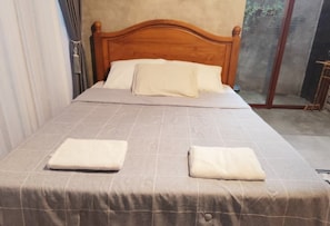 A single bed with a wooden headboard, a grey checkered bedspread, and two white pillows. - nDalem Riyartan Villa Kaliurang (Sleman)