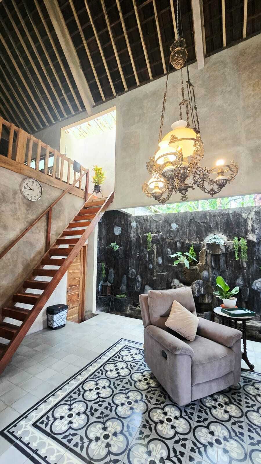 Uma escadaria com corrimãos de madeira, um candelabro, uma poltrona cinza e um piso com padrão.