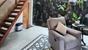 Una escalera con barandillas de madera, un candelabro, un sillón gris y un suelo con estampado.