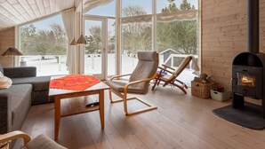 A cozy room with a wooden ceiling, a fireplace, a sofa, a table, and a chair. - 4 Star Holiday Home in Nykobing Sj (Nykobing Sjaelland)