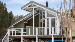 A cabin with a sloped roof, large windows, a covered porch, and a stack of firewood outside. - 4 Star Holiday Home in Nykobing Sj (Nykobing Sjaelland)