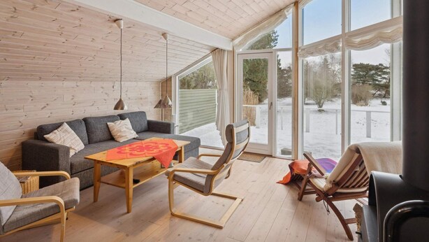 A cozy room with a wooden ceiling, a grey sofa, a wooden table, and a rocking chair. - 4 Star Holiday Home in Nykobing Sj (Nykobing Sjaelland)