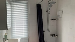 A bathroom with a bathtub, shower, sink, and window with blinds.