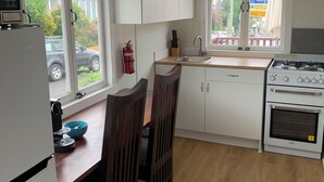 A compact kitchen with white cabinets, a stove, a sink, and a dining table with chairs.