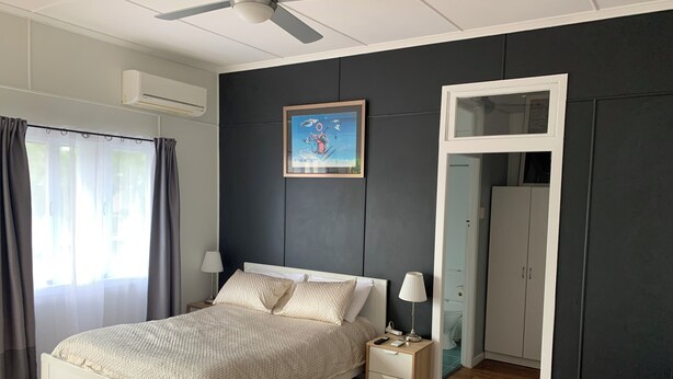 A bedroom with a bed, bedside tables, a ceiling fan, a painting, and a wardrobe.