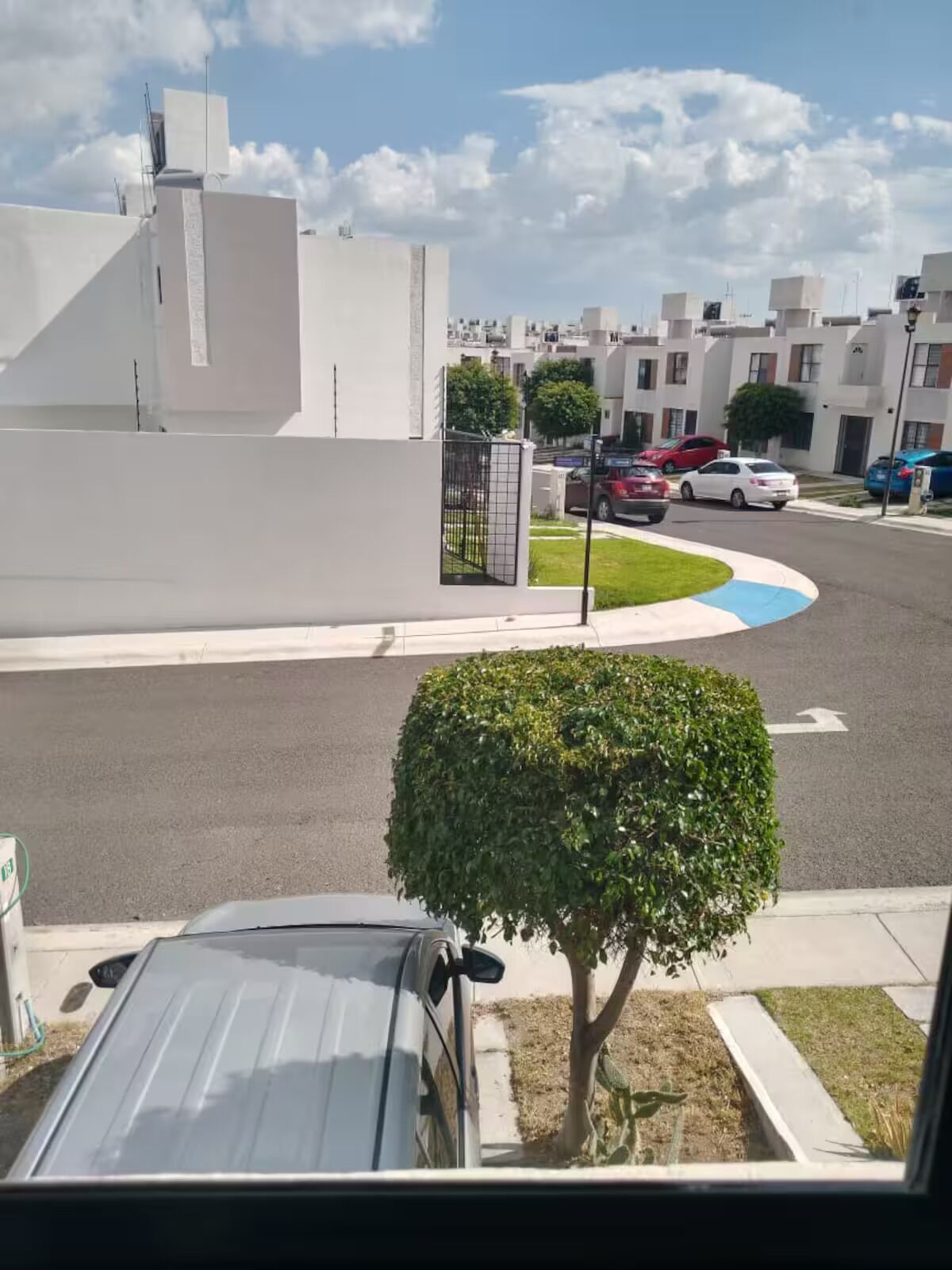 Une rue résidentielle bordée d’immeubles blancs, avec des voitures garées et un arbre au premier plan.