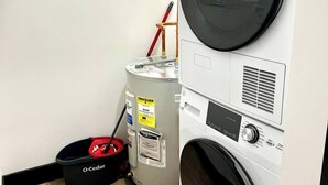 Uma lavanderia com máquinas de lavar e secar empilhadas, um aquecedor de água e um balde vermelho.