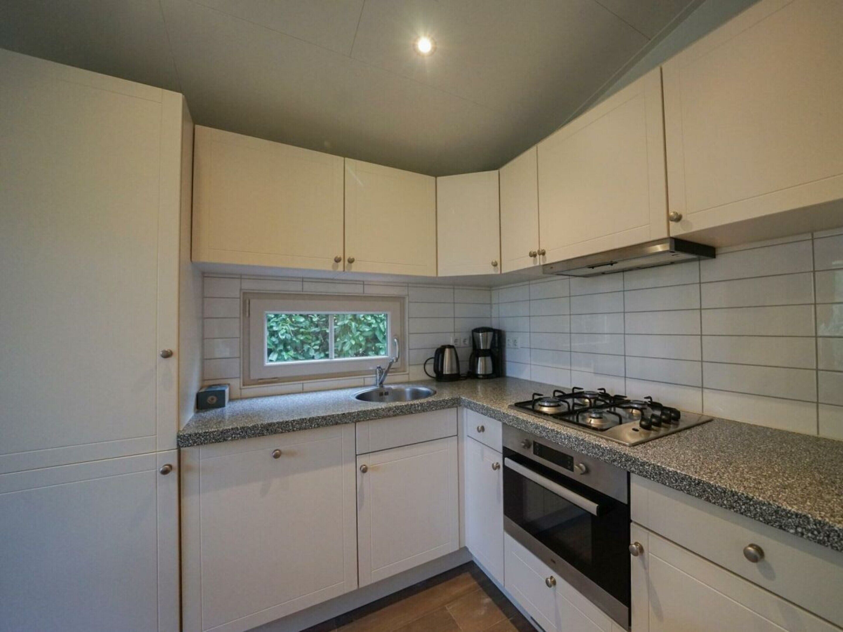 A kitchen with white cabinets, a window, a sink, a stove, and a coffee maker.