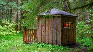 Eine Holzhütte im Wald mit einer kleinen Terrasse und einem Fenster mit rötlicher Verglasung.