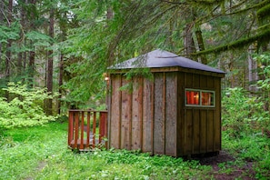 A wooden cabin in a forest with a small deck and a window with red-tinted glass.