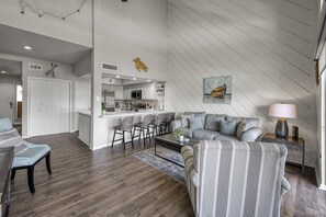 Ein modernes Wohnzimmer mit grauem Sofa, einem gestreiften Sessel und einem Essbereich mit Holztisch.