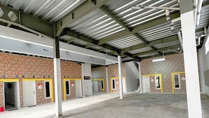 Um espaço interno amplo, com piso de concreto, vigas de metal e várias portas com molduras amarelas.