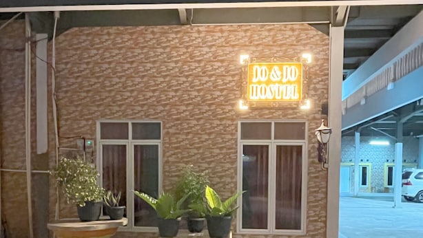 Um hostel com um letreiro de neon, plantas em vasos e uma janela.