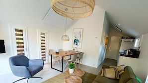 Un soggiorno moderno con un divano, una poltrona blu, un tavolo da pranzo con sedie, un lampadario e un angolo cottura sullo sfondo.