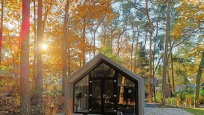 Una moderna casa in vetro con tetto triangolare, immersa in una foresta dai colori dell'autunno.