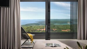A bedroom with a large window, a bed, a chair, and a plant. -  Villa Panoramica (Rabac)