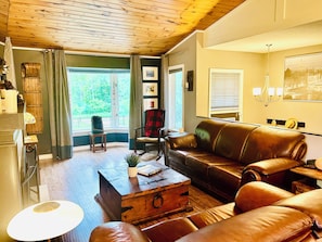 Un salon avec un plafond en bois, un canapé en cuir, une table basse en bois et une vue sur la verdure à l’extérieur.