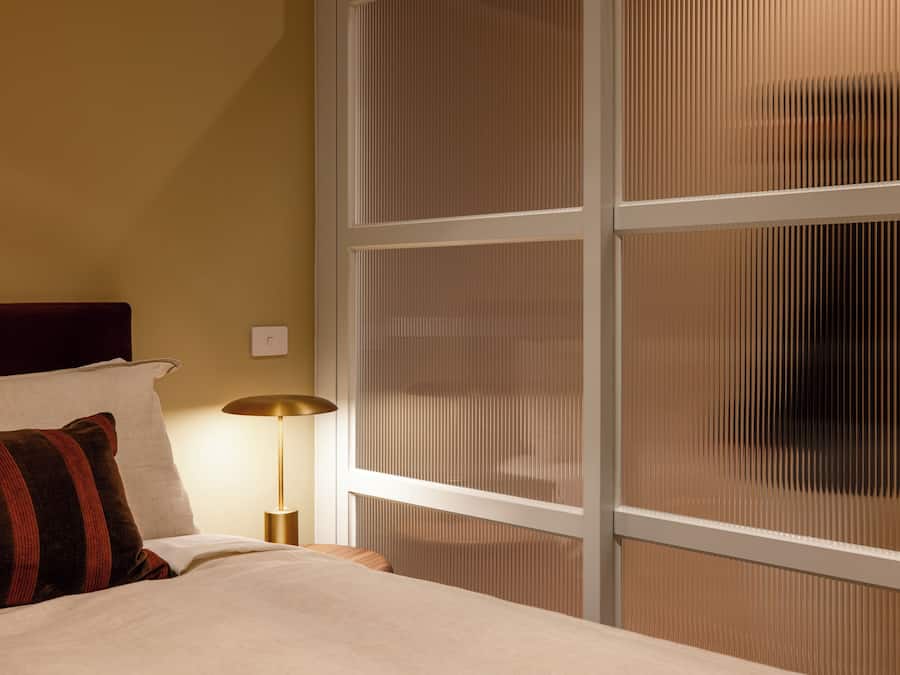 Una habitación de hotel con cama, mesita de noche, lámpara y ventana con persianas.