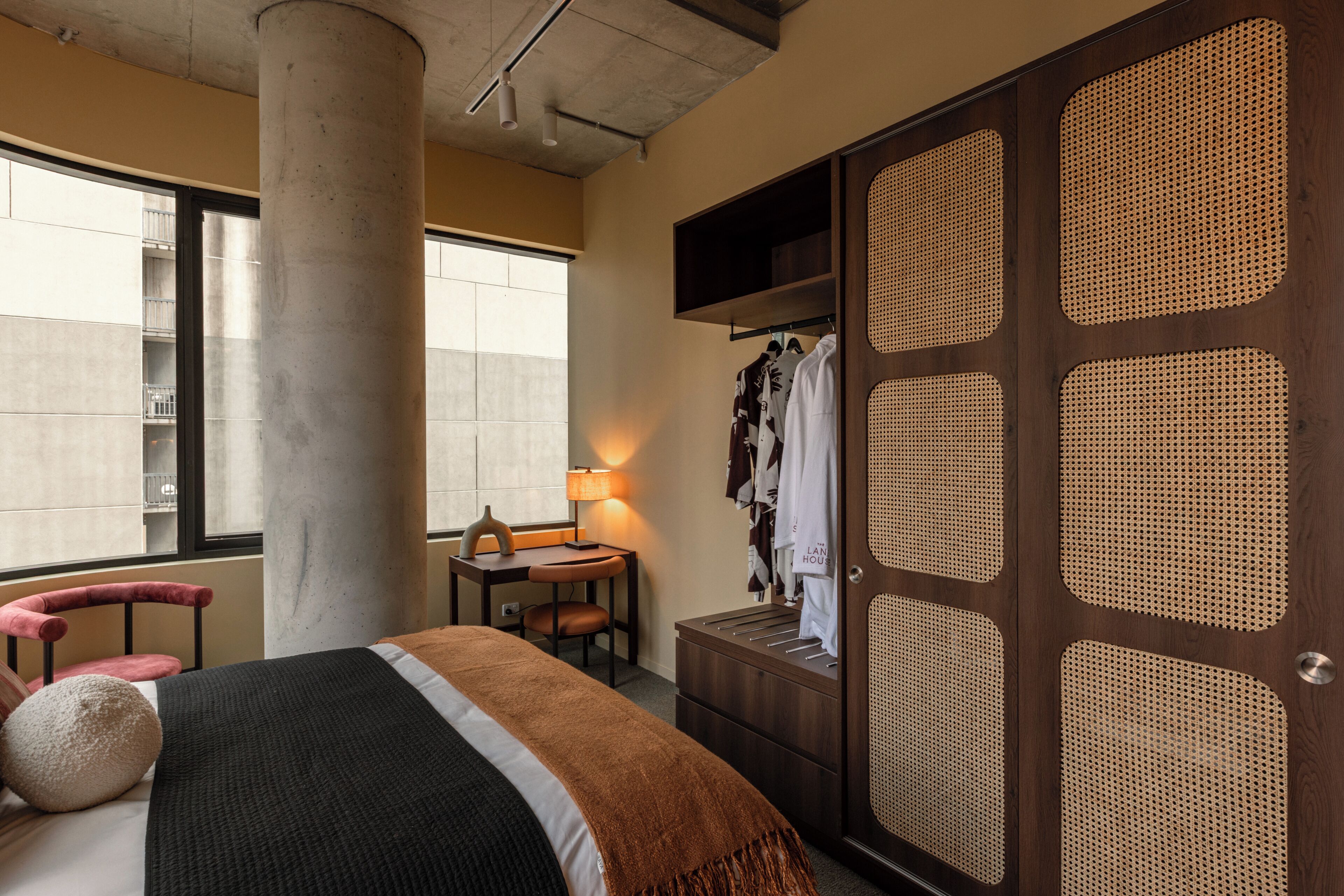Habitación de hotel con cama, una silla, escritorio, lámpara y armario con puerta de tejido.