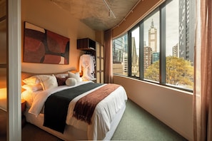 Ein Hotelzimmer mit großem Bett, Blick auf die Stadt, einem Gemälde an der Wand und einem Vorhangfenster.