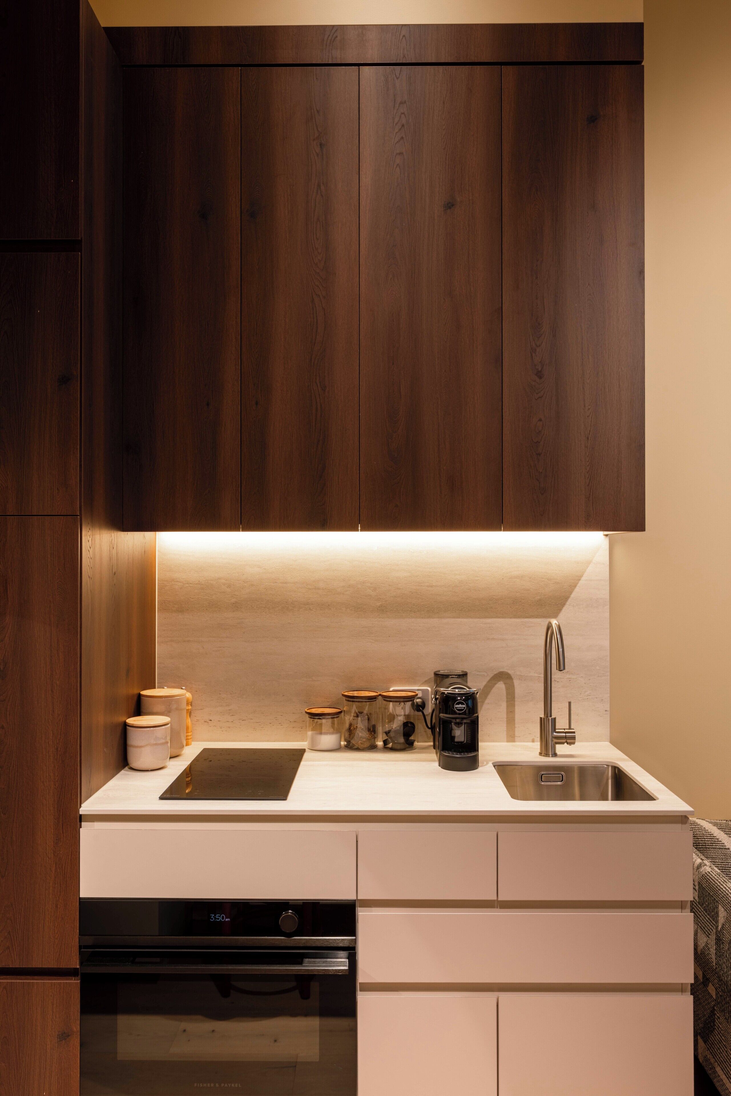 Una cocina con armarios de madera, encimera blanca, pileta de acero inoxidable, cafetera y lavavajillas.