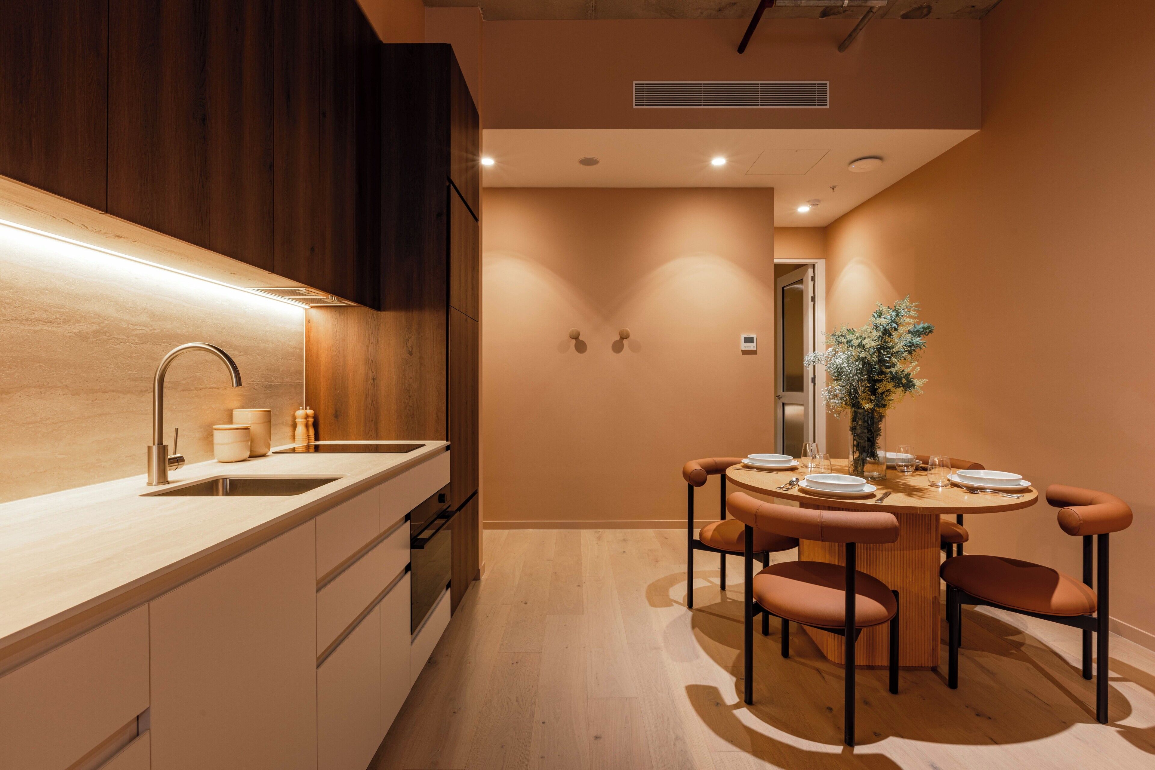 A modern kitchen with a central island, wooden cabinets, and a dining area with a round table and chairs.