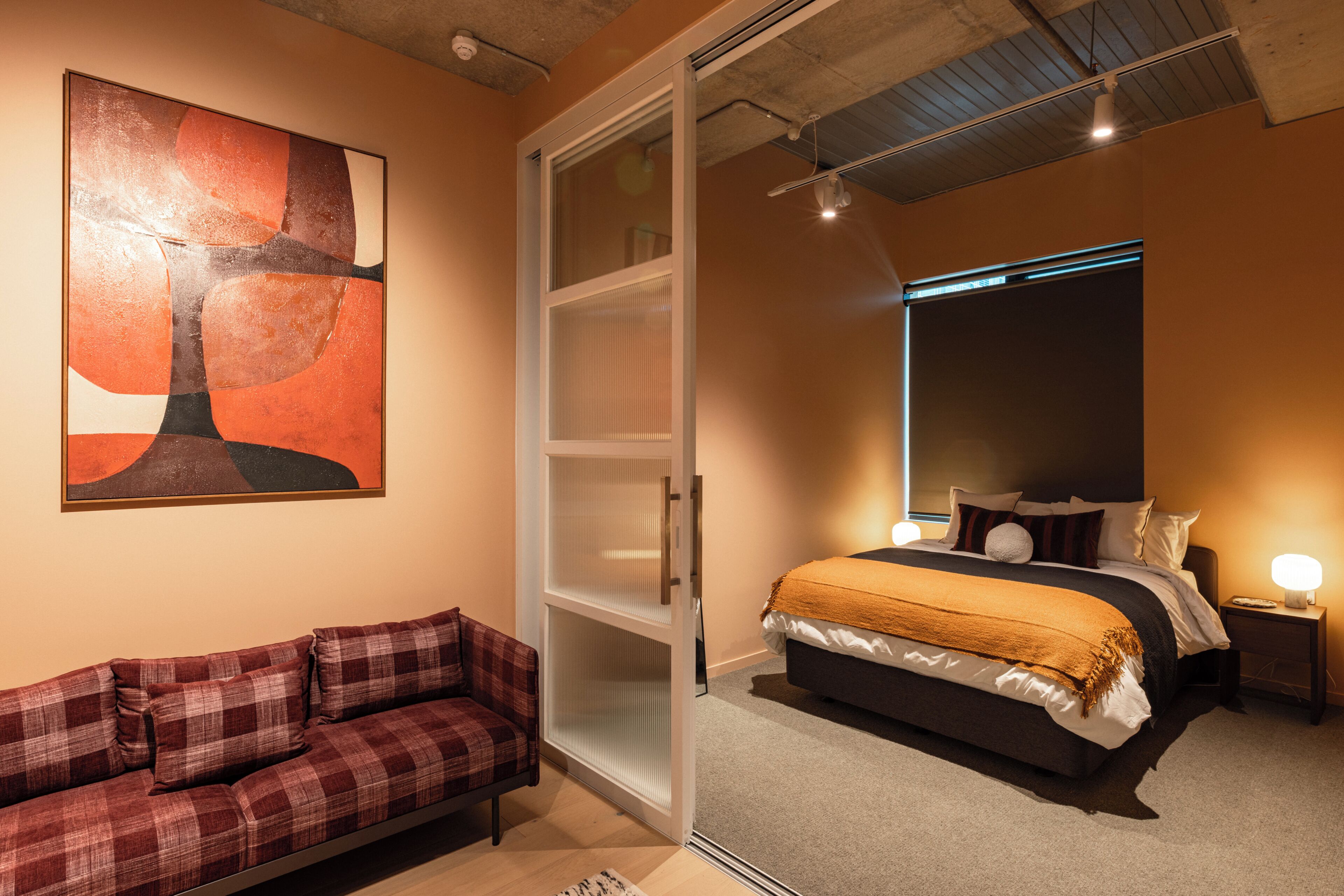 Un dormitorio con cama, mesita de noche, lámpara, sofá y un cuadro en la pared.