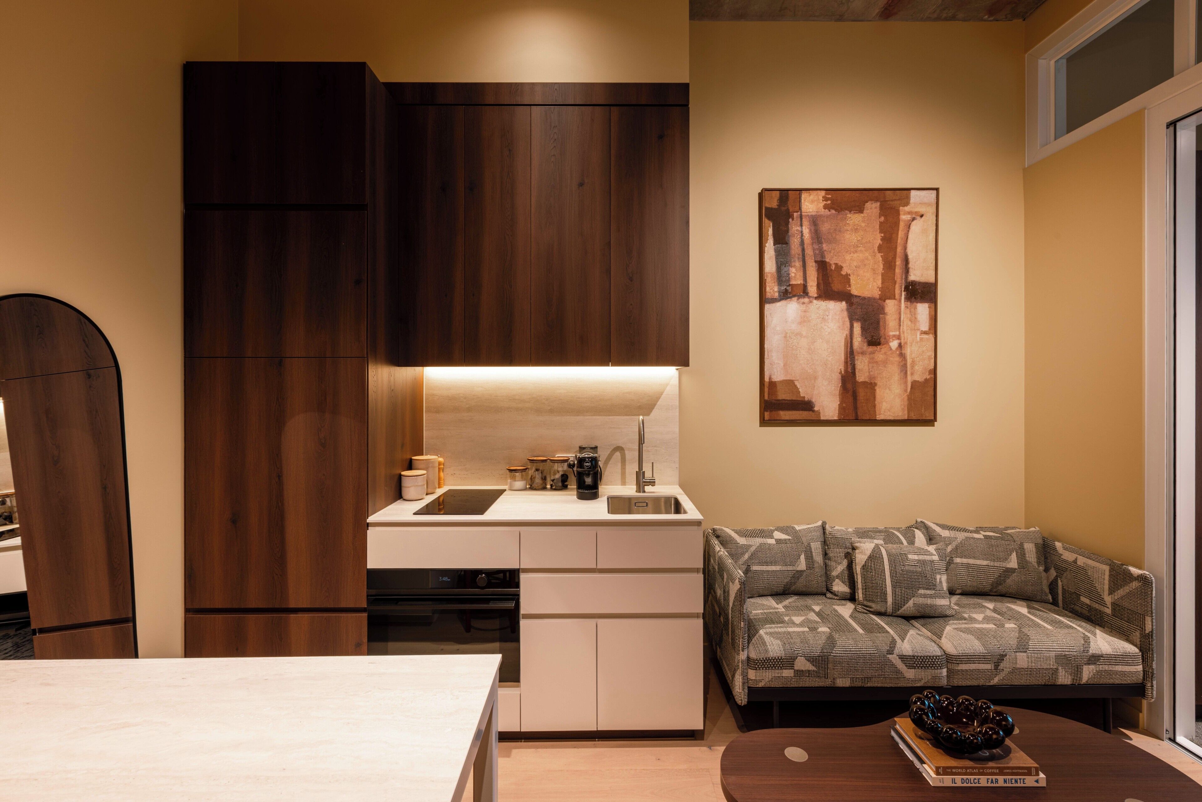 A compact kitchen with a built-in oven, a sink, and a dining area with a table and sofa.