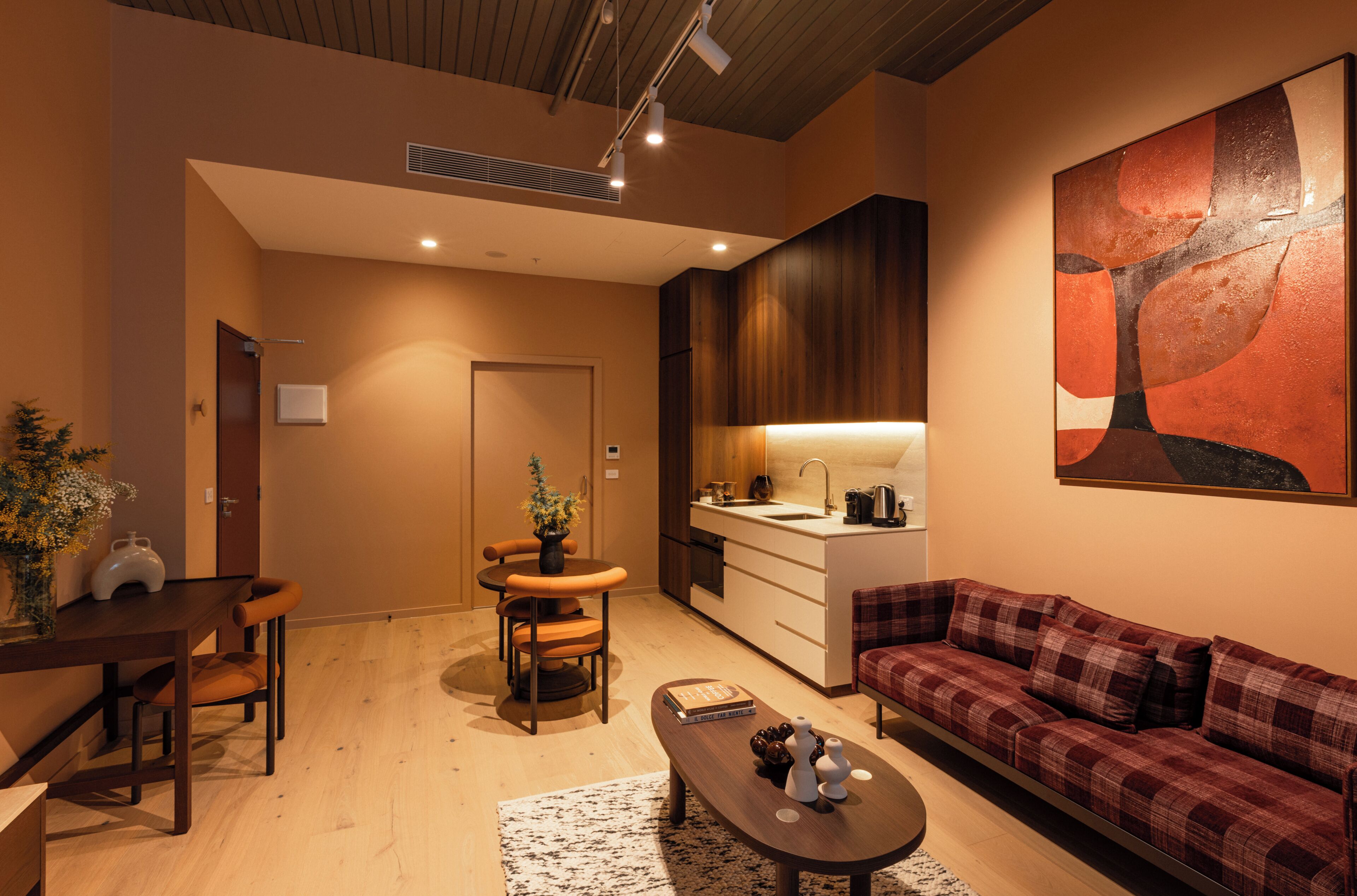 Una sala moderna con un sofá, una mesa de comedor con sillas, una zona de cocina con un fregadero y un cuadro abstracto grande en la pared.