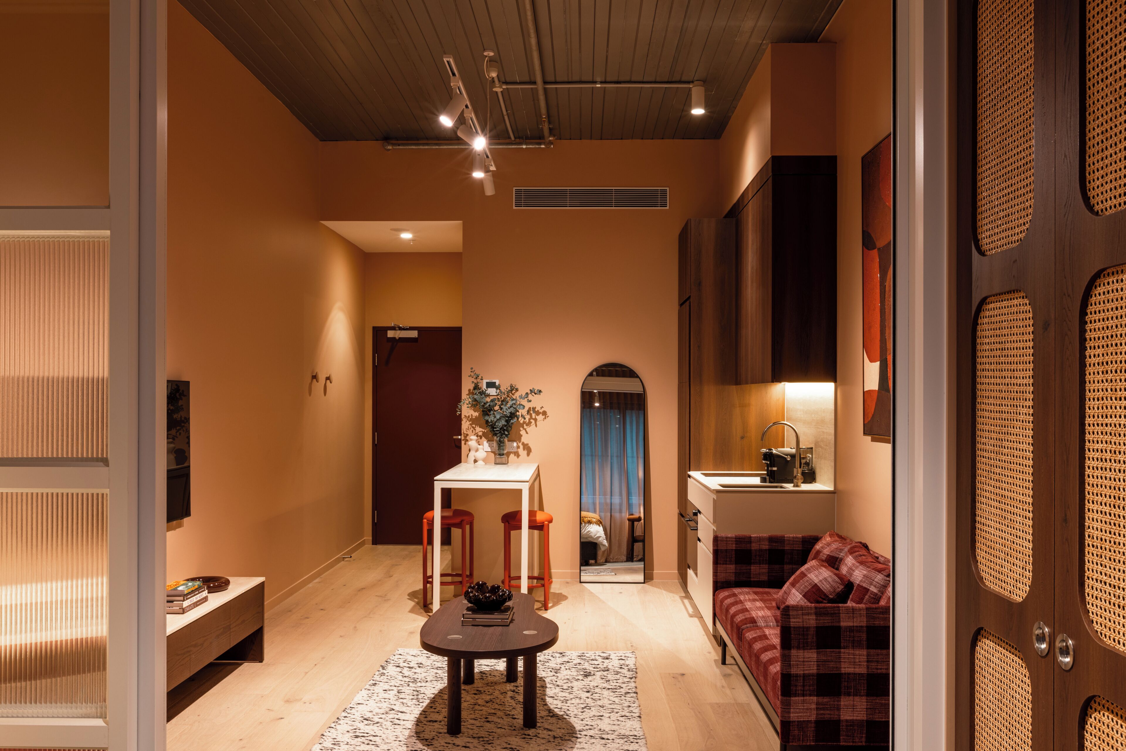 A modern interior with a wooden ceiling, a dining area with a table and chairs, a sofa, and a kitchen area with a sink and countertop.