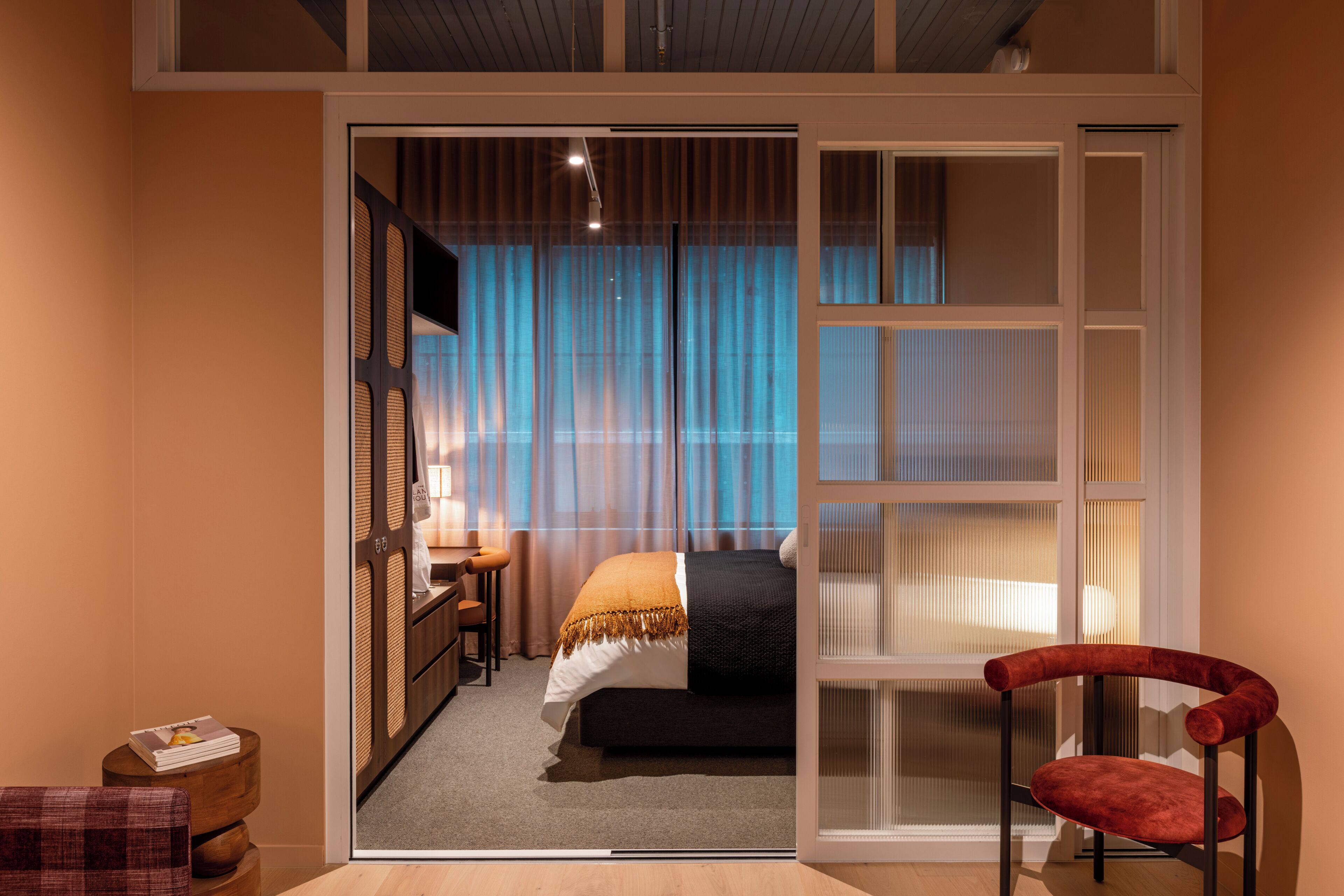 Habitación de hotel con cama, escritorio, silla y vistas a través de una puerta corrediza.