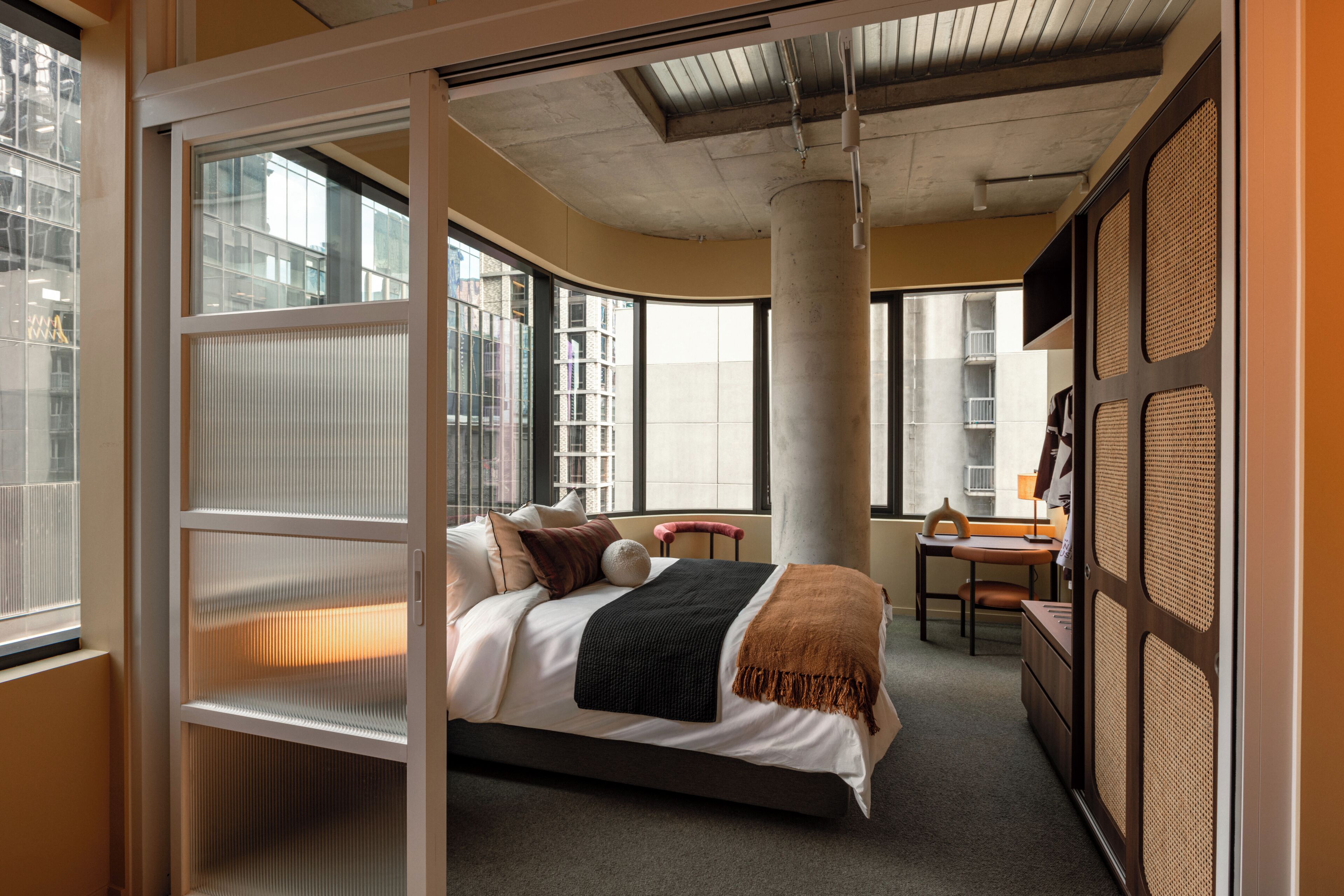 A modern hotel room with a bed, a desk, and a large window.