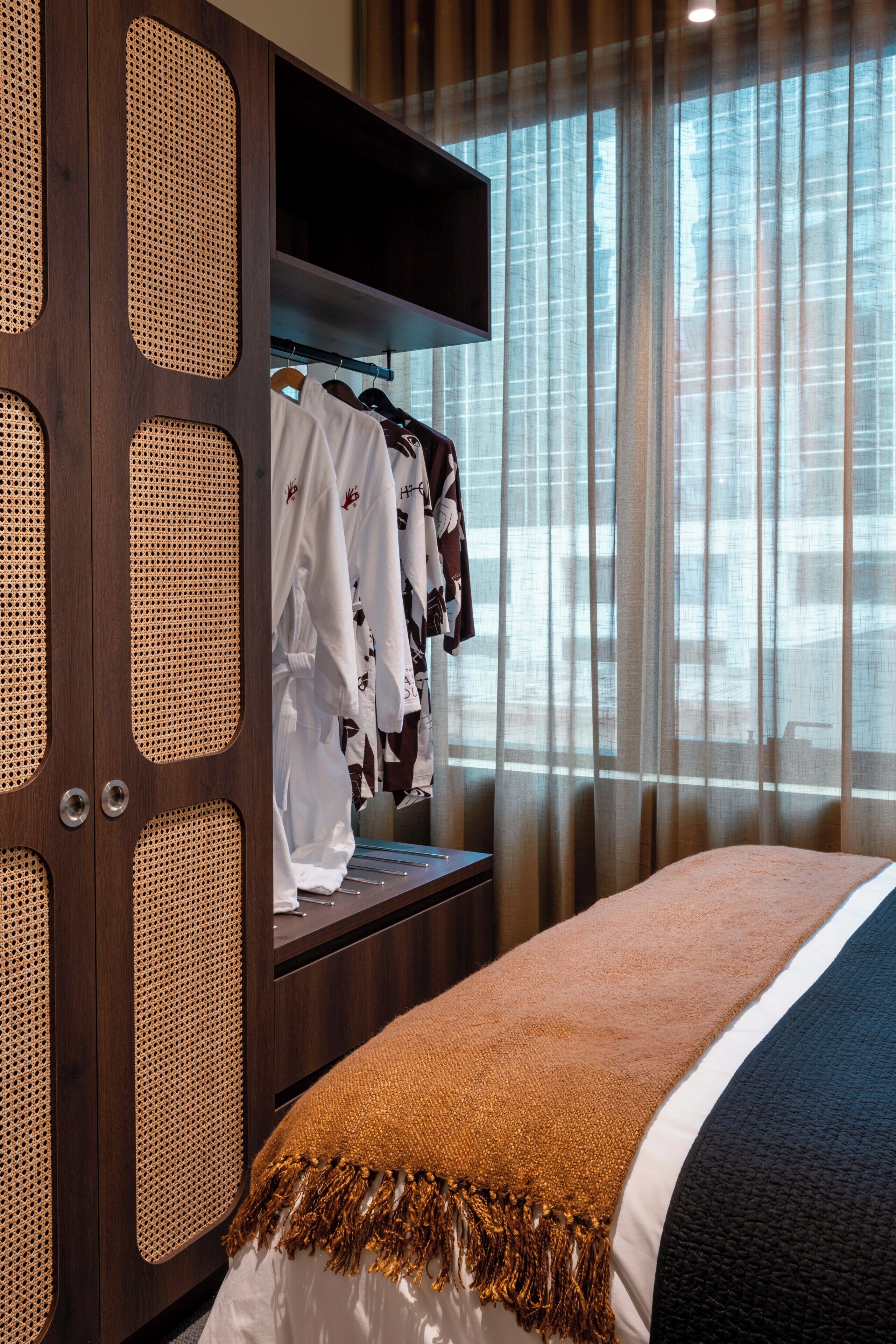 Habitación de hotel con cama, armario de diseño trenzado y ventana con cortinas.
