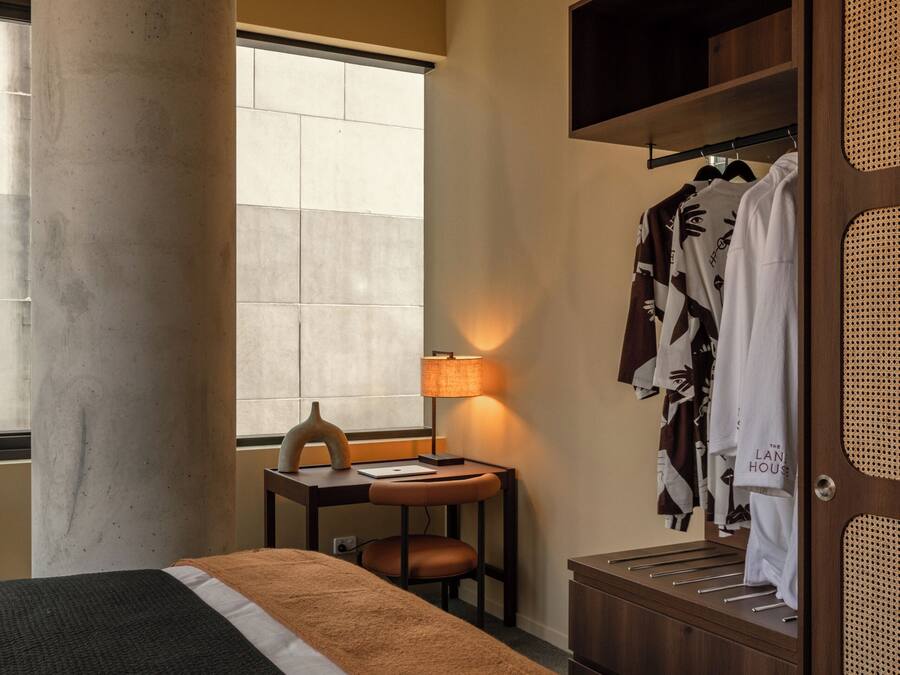 Una habitación de hotel con una cama, un escritorio con lámpara, un armario y una ventana.