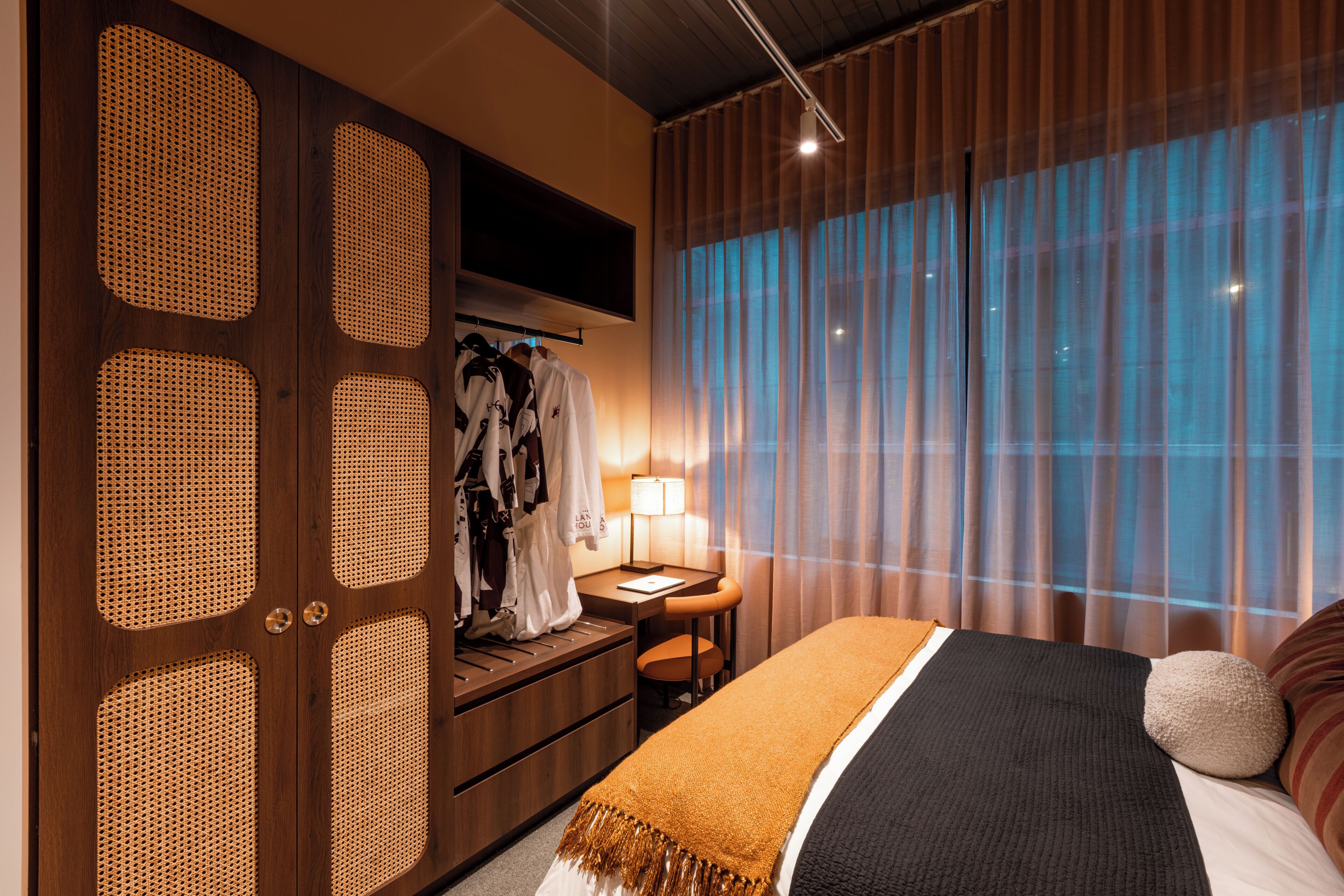 A hotel room with a bed, a desk, a wardrobe, and a large window with curtains.