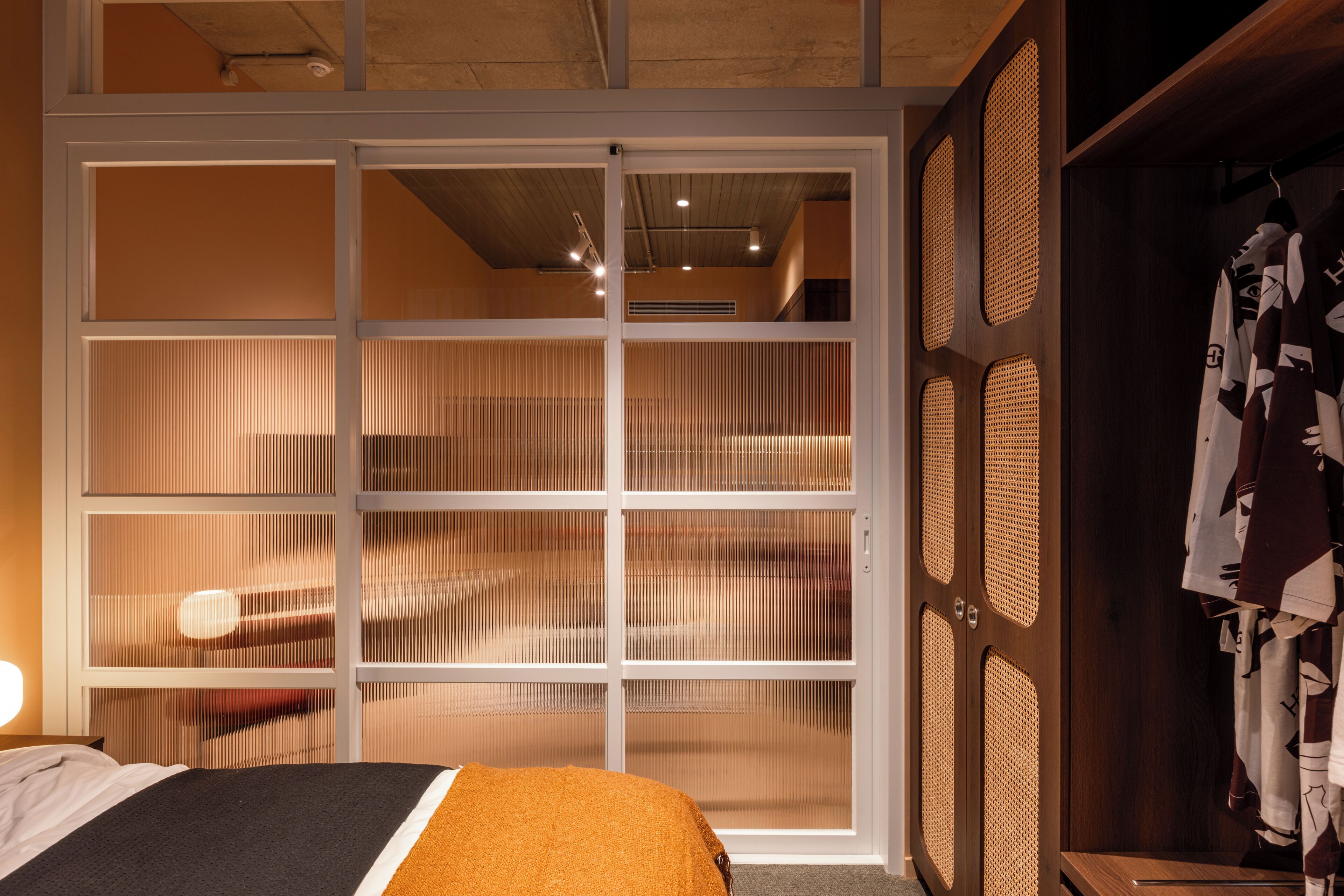 A hotel room with a bed, a wardrobe, and a sliding door with vertical blinds.
