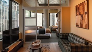 A modern living room with a flat-screen TV, a sofa, a dining area, and a bedroom with a bed and a desk. - The Lane House (Melbourne)