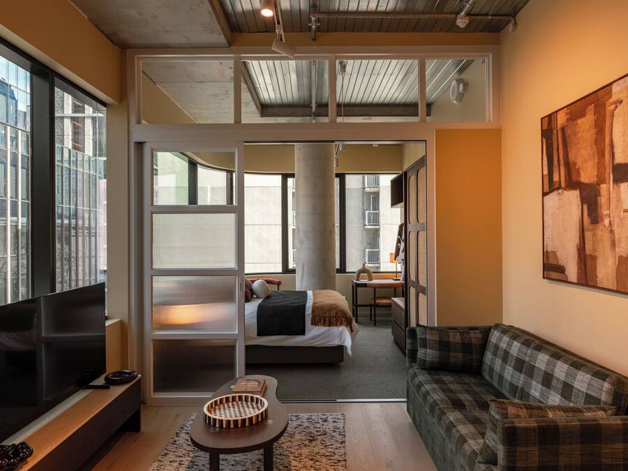 A modern living room with a flat-screen TV, a sofa, a dining area, and a bedroom with a bed and a desk.