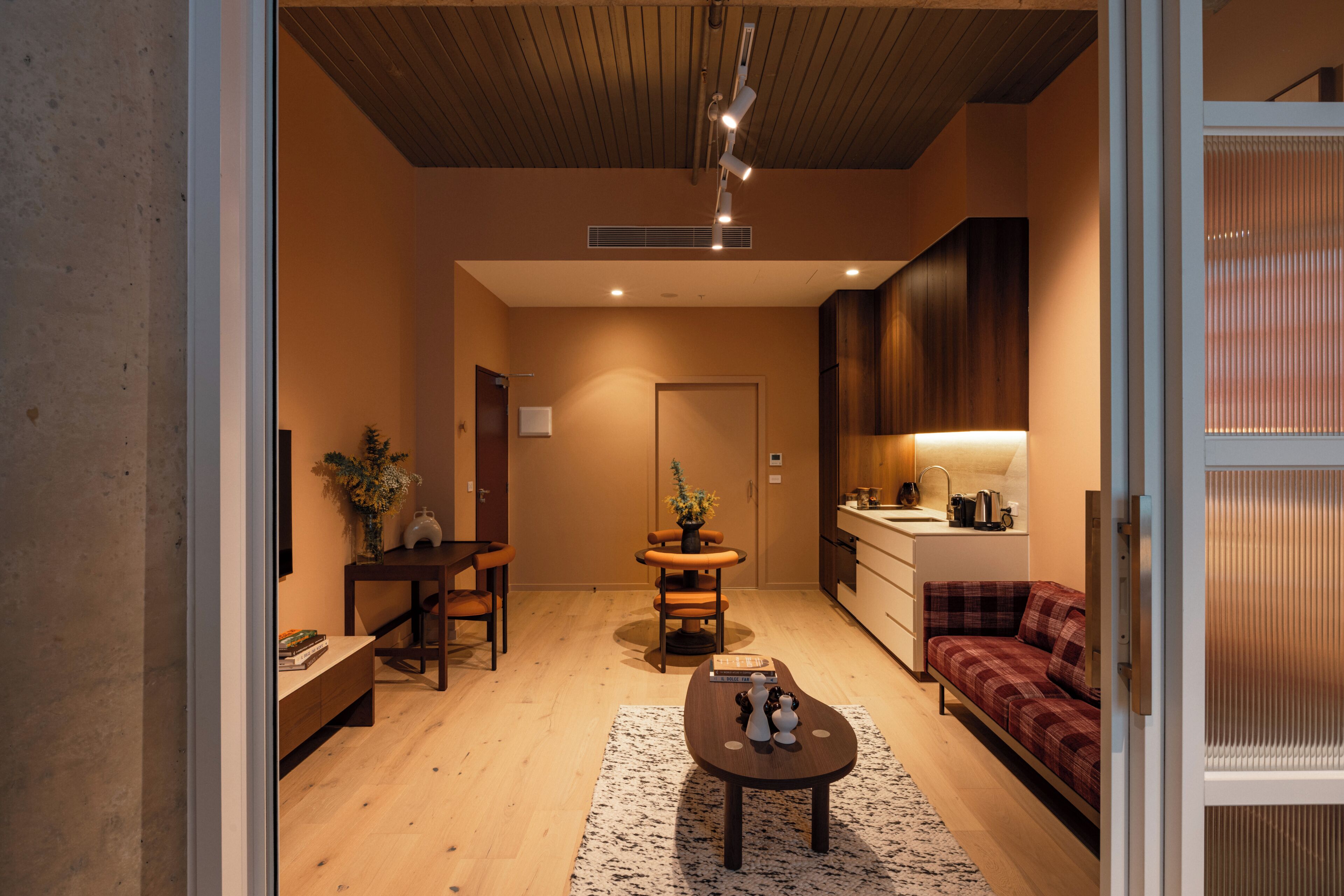 A modern living room with a wooden floor, a sofa, a dining table with chairs, and a kitchen area with cabinets and a sink.