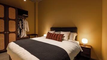 A neatly made bed with a black and white bedspread, two bedside lamps, and a wooden wardrobe with a woven design.